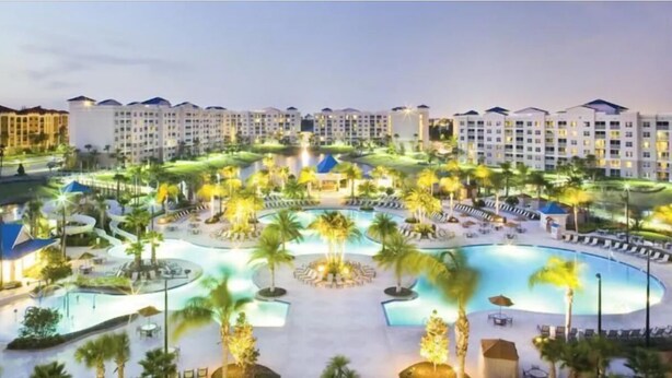 Een resort met meerdere gebouwen, een centraal gelegen zwembad en omliggende palmbomen.