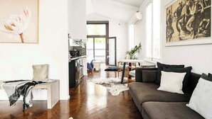 A modern living room with a dark grey sofa, a small white table, and a kitchen in the background.