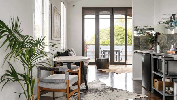 A modern kitchen with a dining area, large windows, and a view of the outdoors.