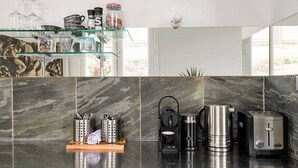 A modern kitchen with a marble backsplash, a glass shelf with kitchenware, and a coffee machine.