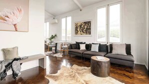 A modern living room with a grey sofa, a round wooden coffee table, and a large painting on the wall.
