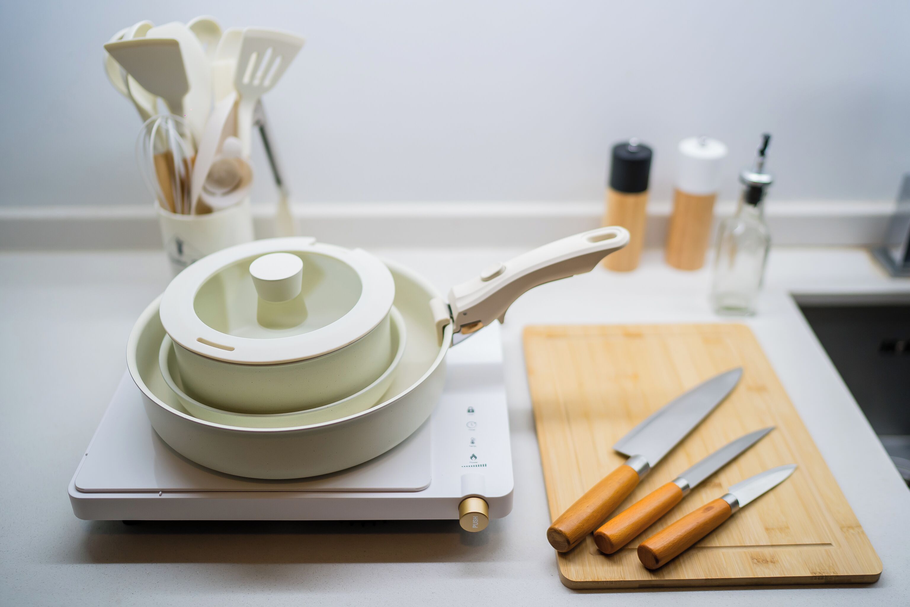 Une cuisine équipée d’une plaque de cuisson à induction moderne, d’une planche à découper avec des couteaux et d’un porte-ustensiles.
