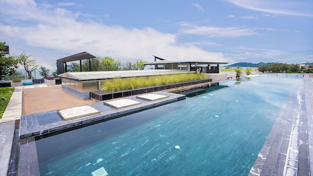 A modern pool area with a clear view of the pool, a wooden deck, and a building with a glass facade. - Beachside Chic Coastal Hideaway (Hua Hin)