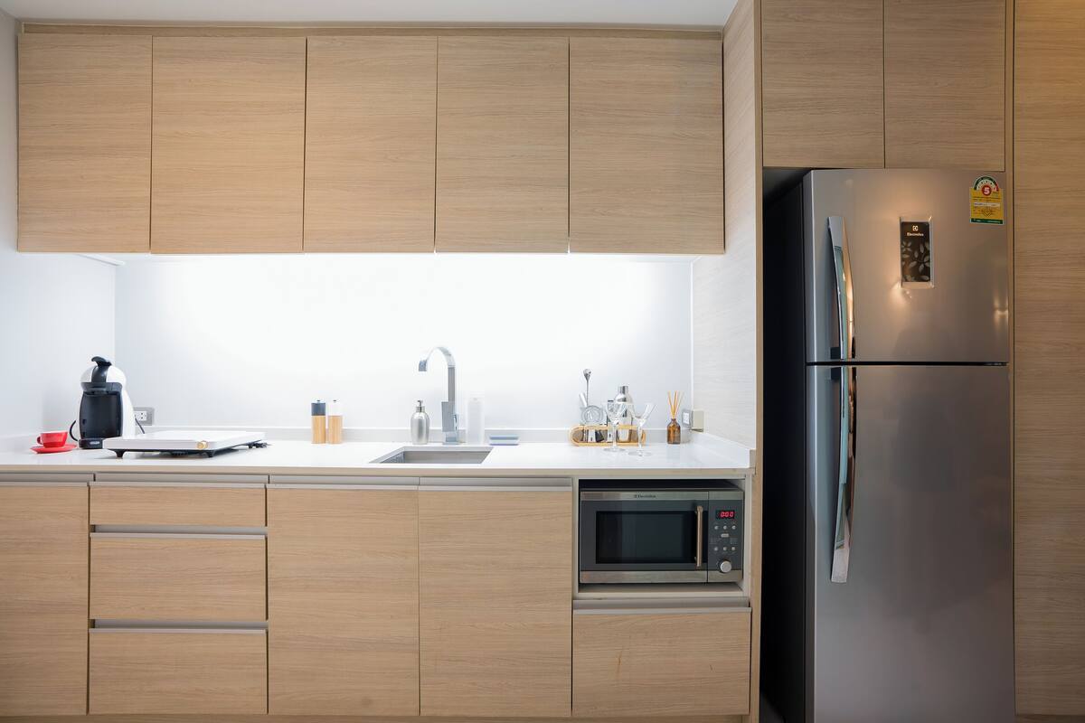 A modern kitchen with wooden cabinets, a stainless steel refrigerator, a built-in microwave, and a coffee maker.