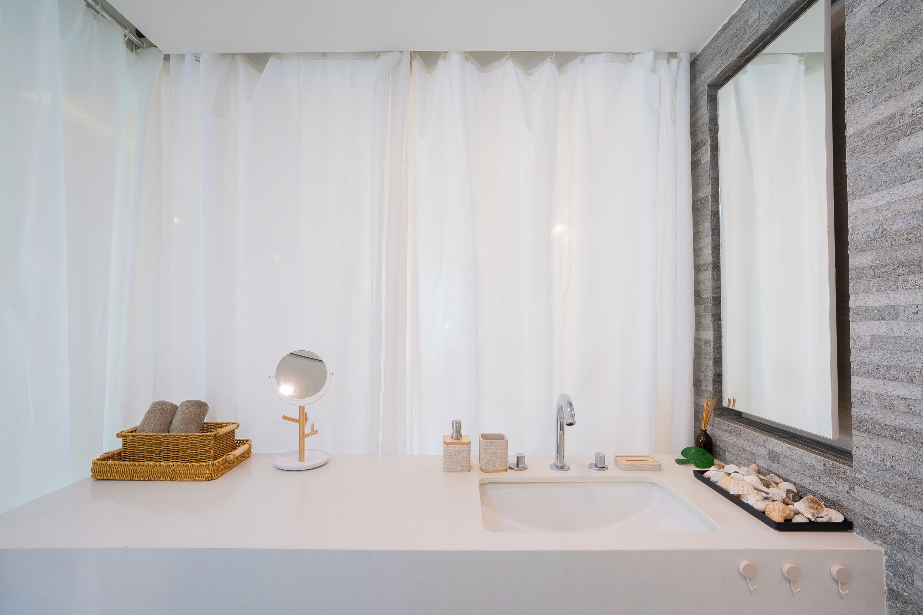 A bathroom with a large mirror, a sink, and a window with curtains.