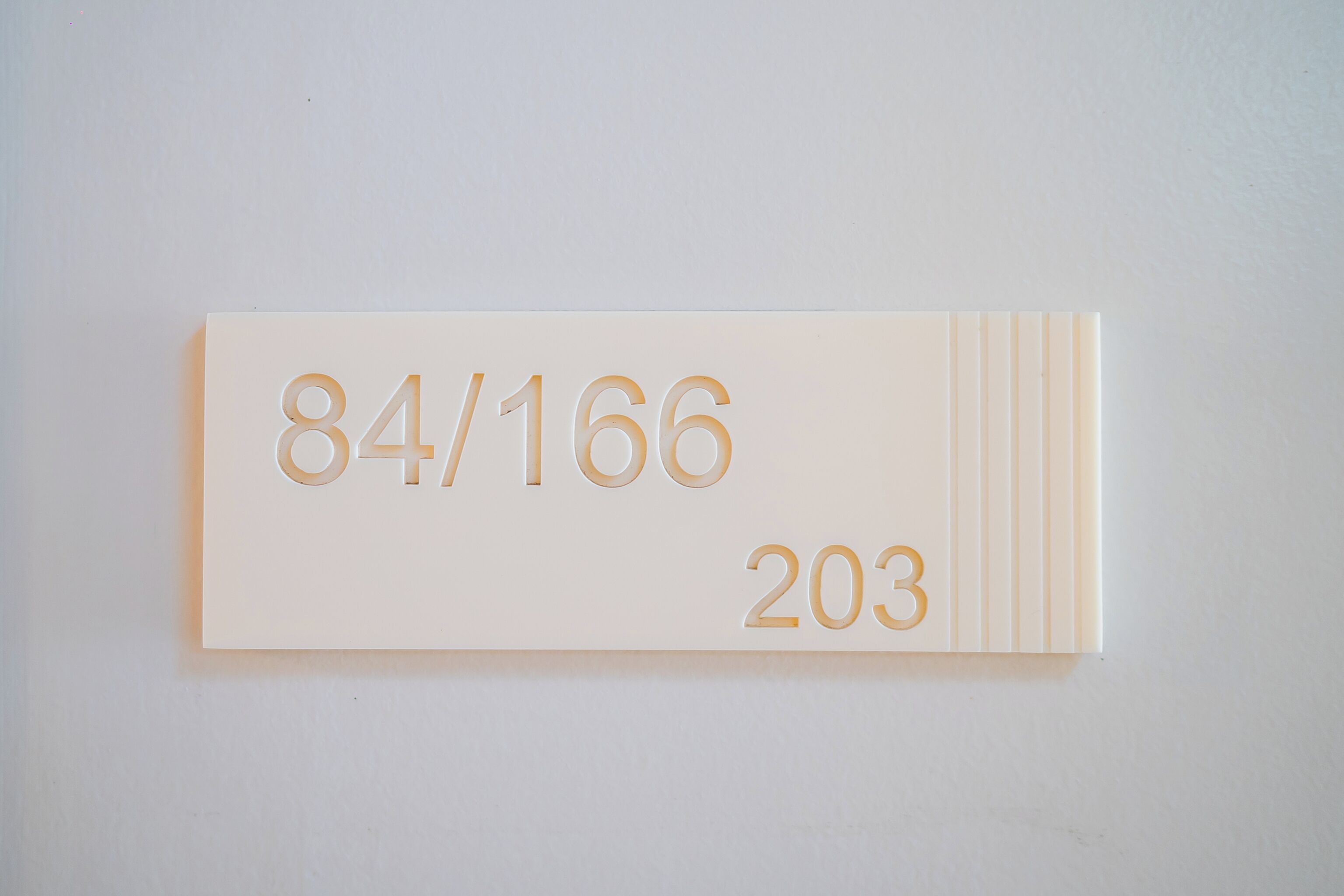 Ein weißes Schild mit den Nummern 84/166 und 203 an einer Wand.