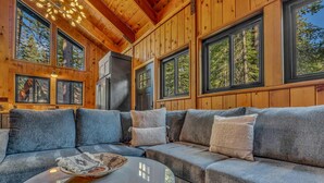 Ein gemütliches Blockhaus-Interieur mit einer Eckcouch, einem runden Couchtisch und großen Fenstern mit Blick auf Bäume.