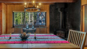 Ein Holzinterieur mit einem für zwei Personen gedecktem Esstisch, einer Chandelüstere und einem Blick ins Freie durch ein Fenster.