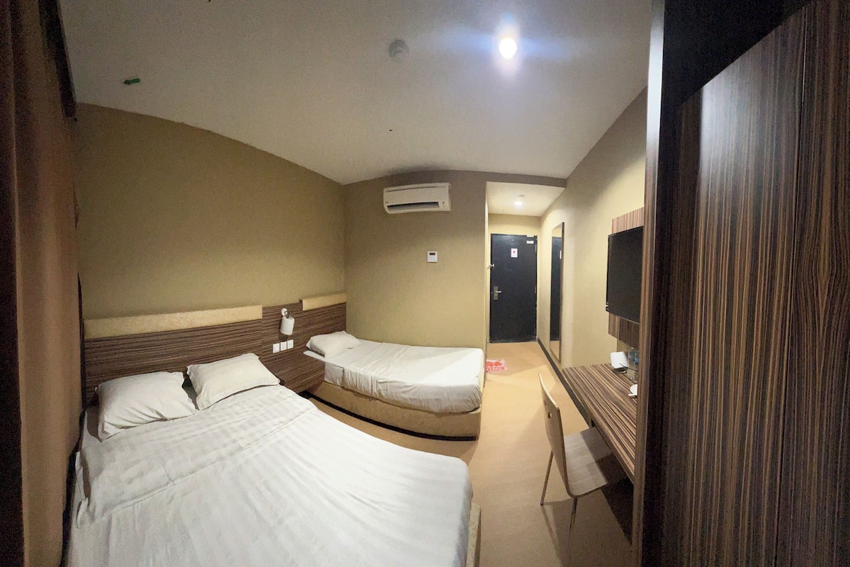 A hotel room with two single beds, a wooden headboard, a flat-screen TV, and a small desk.