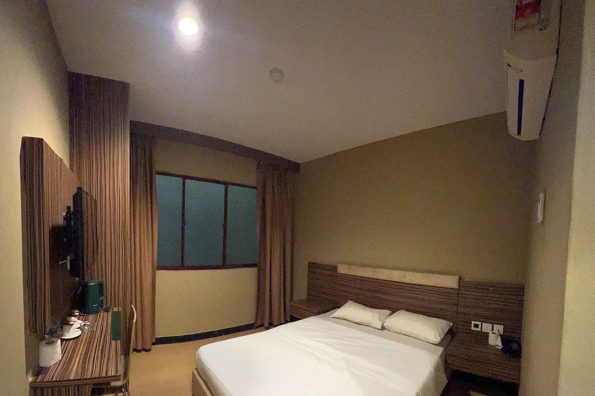 A hotel room with a bed, a desk with a chair, a TV, and a window.