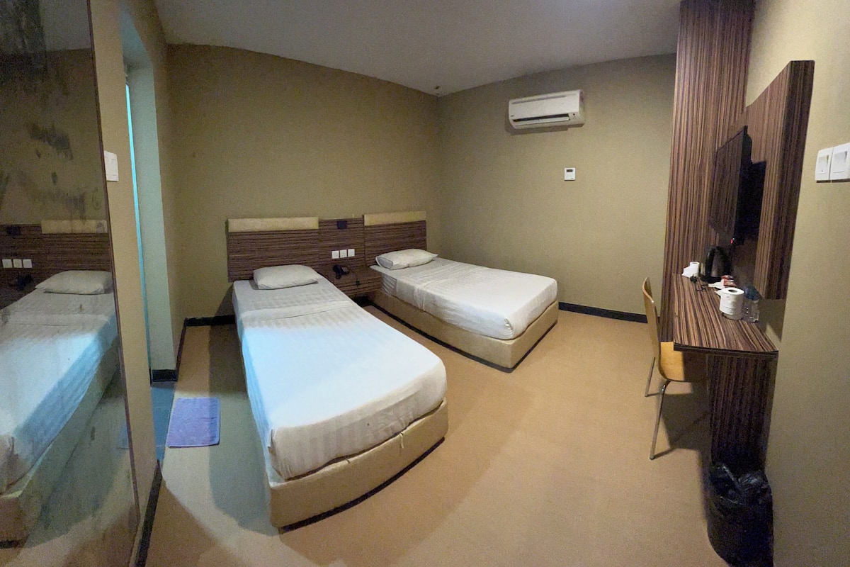 A hotel room with two single beds, a wooden wardrobe, a mirror, and an air conditioning unit on the wall.