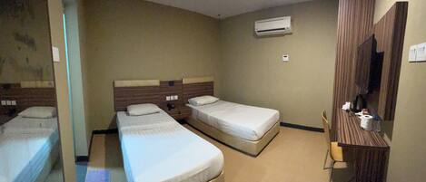 A hotel room with two single beds, a wooden wardrobe, a mirror, and an air conditioning unit on the wall.