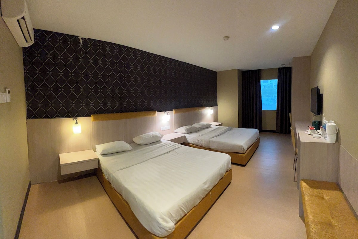 A hotel room with two beds, a desk, a TV, and a patterned wall.