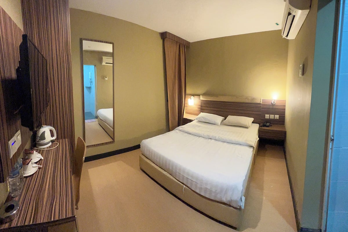 A hotel room with a bed, a bedside table with a lamp, a mirror, and a wall-mounted air conditioner.