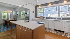 A modern kitchen with a central island, white cabinetry, and a large window providing natural light.