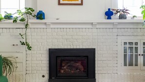 A living room with a white brick fireplace, a round table in the foreground, and a colorful rug.