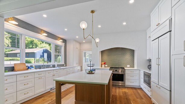 A modern kitchen with white cabinetry, a central island, and a brick backsplash.