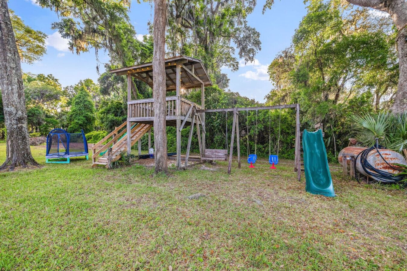 A wooden play structure with a slide, swings, and a small treehouse.