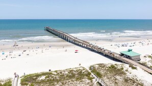 A beach with a long pier extending into the ocean, sandy beach, and a small building with a green roof. - Florida Riverfront Sunrise | Fish, Boat, Unwind (Jacksonville)