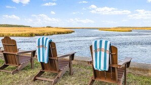 Three Adirondack chairs with striped towels, positioned by a calm river with a grassy bank and a clear sky. - Florida Riverfront Sunrise | Fish, Boat, Unwind (Jacksonville)