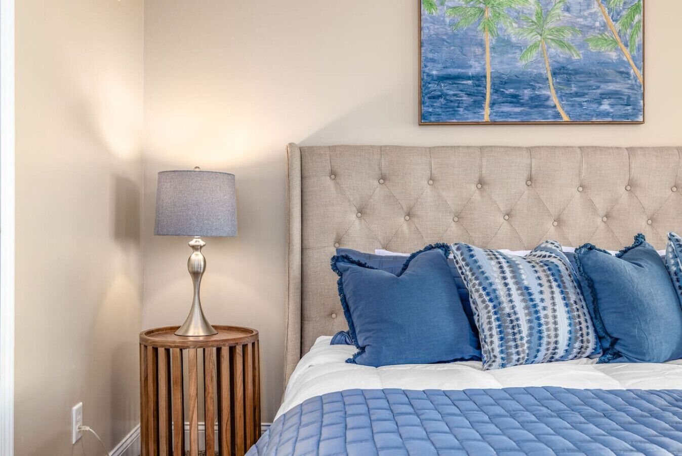 Ein Schlafzimmer mit einem gebügelten Kopfteil, einem Bett mit blauer Bettwäsche und einem Nachttisch mit einer Lampe.