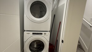 Un lavadero con dos lavadoras Whirlpool apiladas y una escoba roja apoyada en la pared.