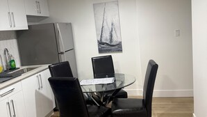 Una cocina moderna con armarios blancos, un refrigerador de acero inoxidable y una zona de comedor con una mesa de vidrio y sillas negras.