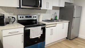 Una cocina moderna con armarios blancos, un microondas de acero inoxidable, una estufa negra, un fregadero y un refrigerador.