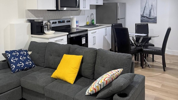 Una sala de estar moderna con un sofá gris, una cafetera y un comedor con mesa y sillas.