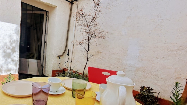 A table set for a meal with plates, glasses, and a pitcher, surrounded by plants and a red chair. - Alhambrita. Cool and quiet house with wifi to disconnect. (Viznar)
