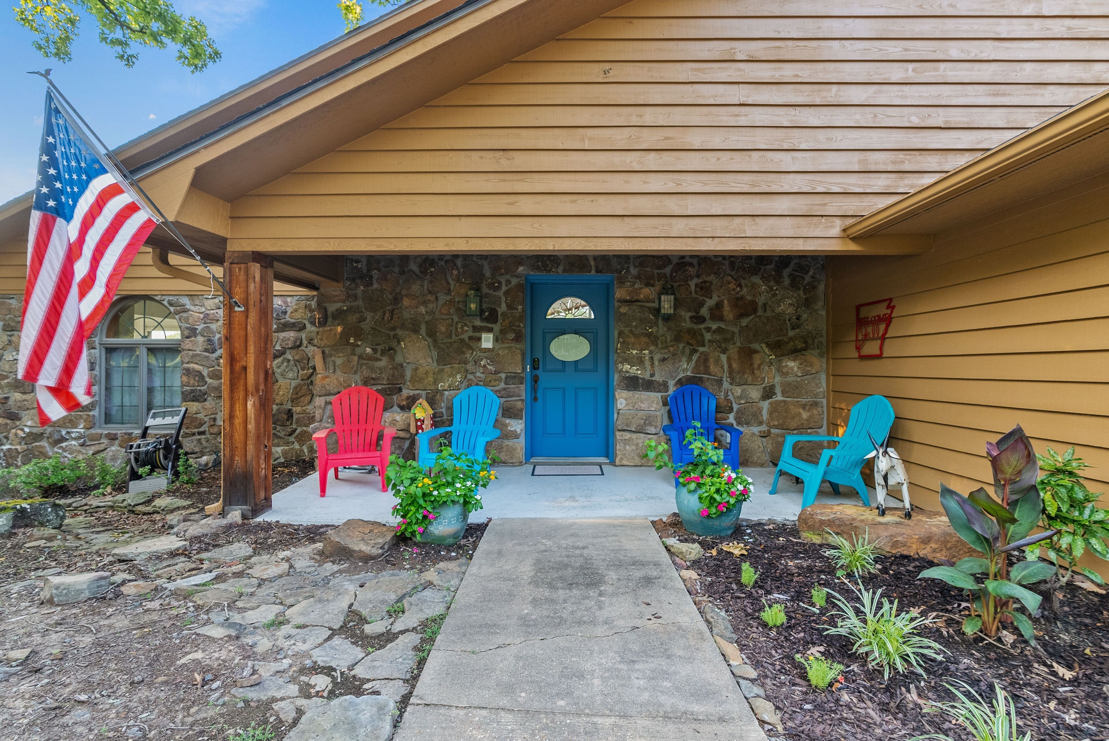 Una casa con fachada de piedra, una puerta azul y un porche con sillas Adirondack de colores.
