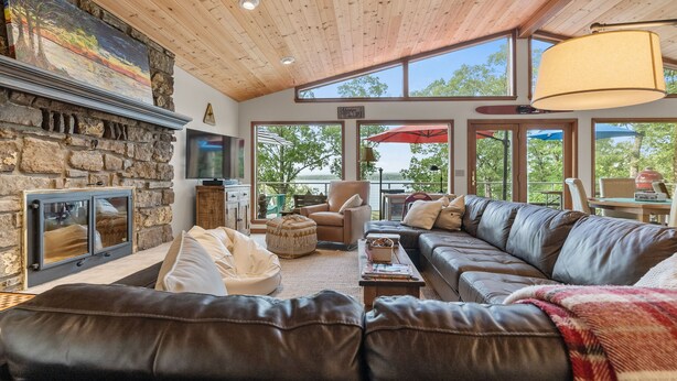 Ein gemütliches Wohnzimmer mit Kamin aus Stein, Ledersofas und großen Fenstern mit Blick ins Freie.