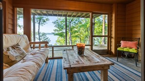 Ein gemütliches Zimmer mit einer hölzernen Bank, einem Tisch mit einem Getränk und Blick auf Bäume und Wasser.
