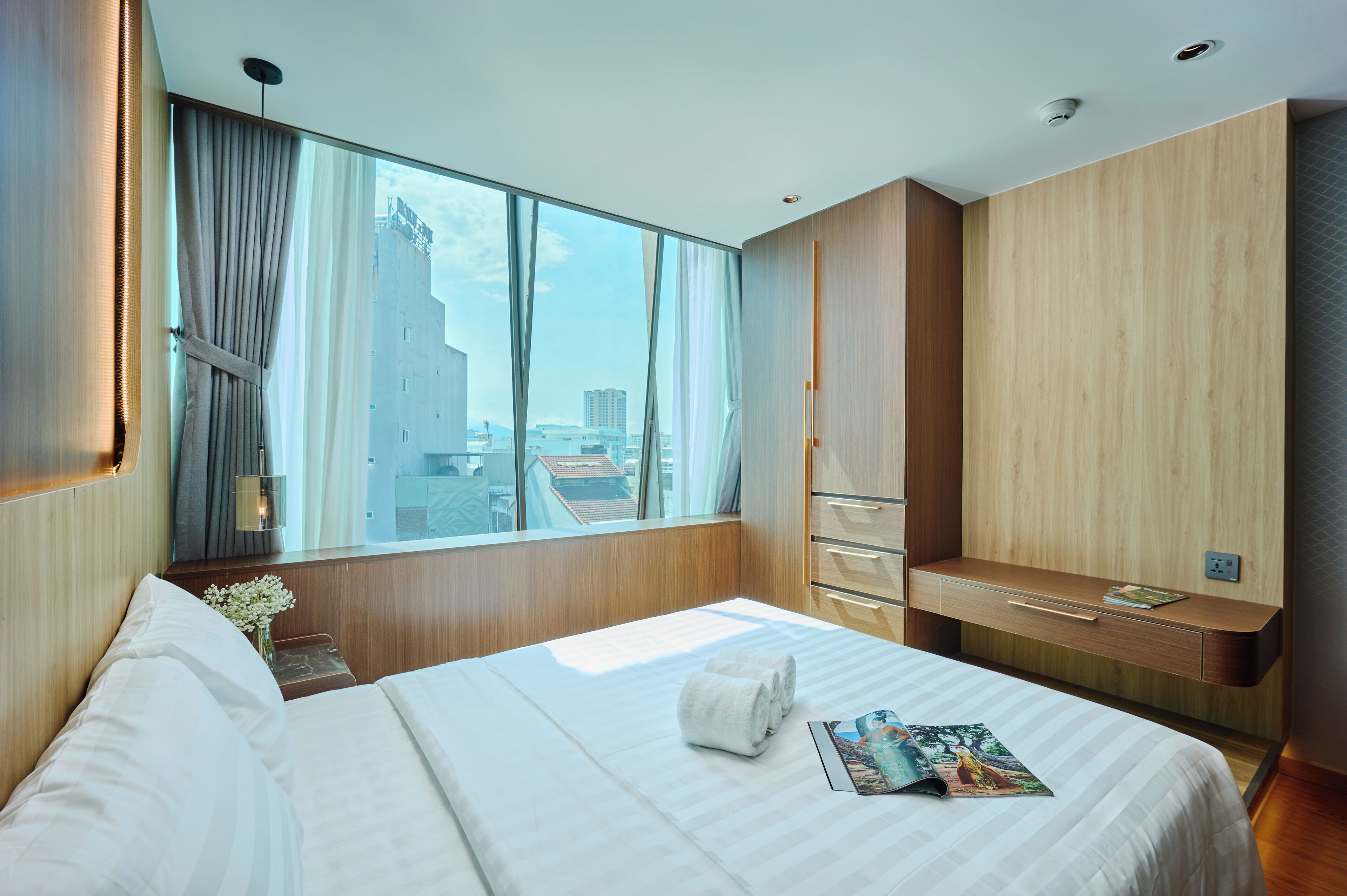 A modern hotel room with a large bed, a wooden desk, and a view of the cityscape.