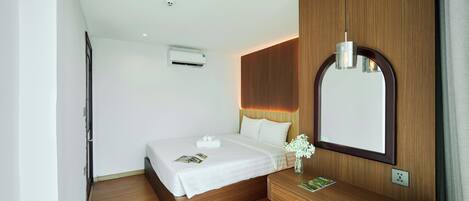 A modern hotel room with a wooden bed, a bedside table, a mirror, and an air conditioning unit.
