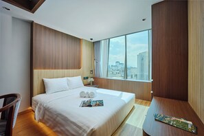 A modern hotel room with a large bed, a wooden headboard, a view of the city through large windows, and a small table with a magazine. - Elite Luxury Hotel & Apartment by Elite24 (Da Nang)