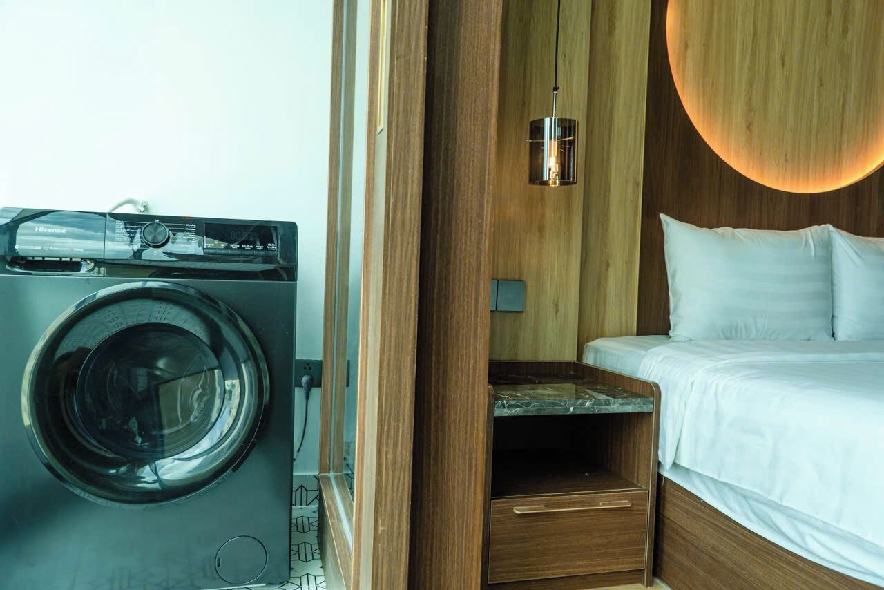 A compact room with a washing machine, a bed, and a wooden cabinet with a hanging light fixture.
