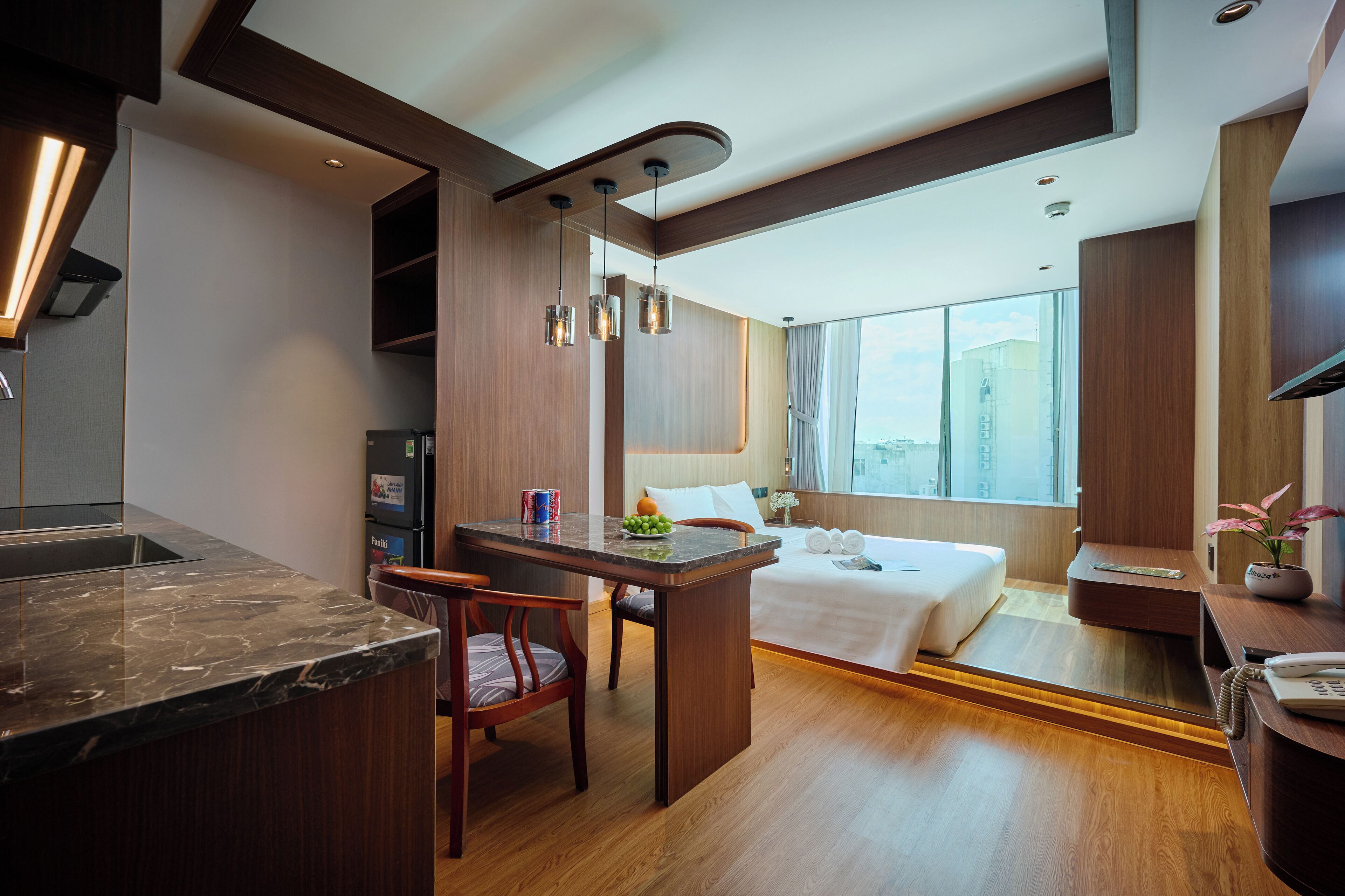 A modern hotel room with a kitchen area, a dining table, and a bed.