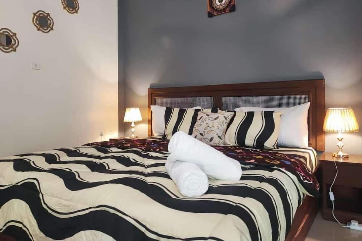 A neatly made bed with striped bedding, two bedside lamps, and a decorative wall piece above the bed.