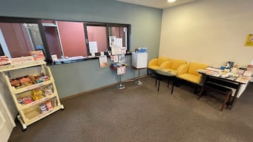 A reception area with a counter, a yellow sofa, a small table, and a vending machine.