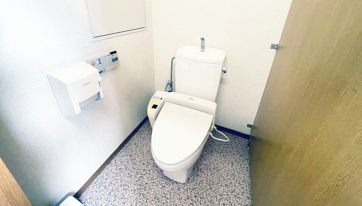 A small, clean bathroom with a toilet, a bidet, and a hand dryer.