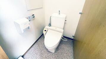 A small, clean bathroom with a toilet, a bidet, and a hand dryer.