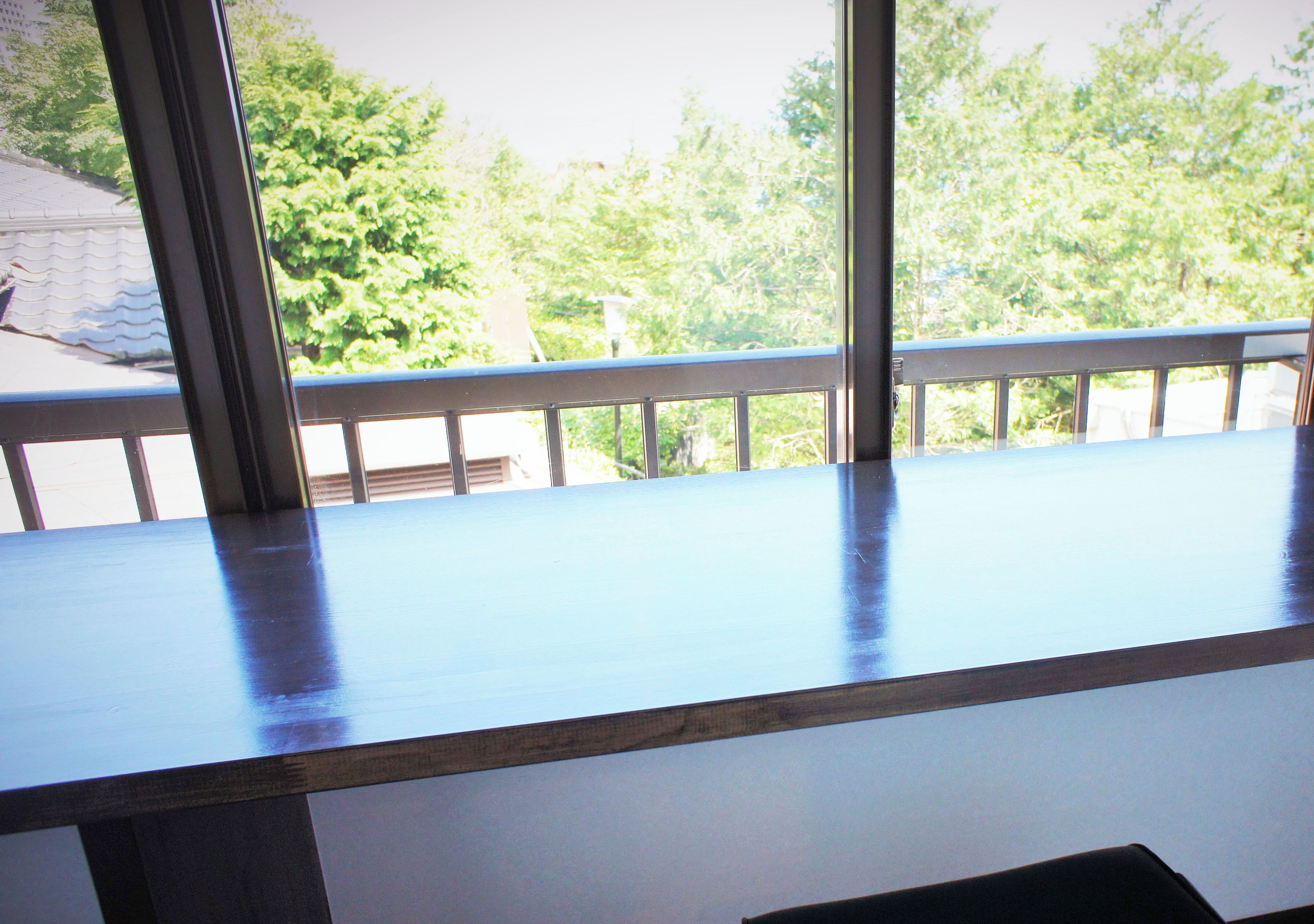 Una habitación con un gran ventanal, una mesa de madera y vistas a árboles y un edificio.