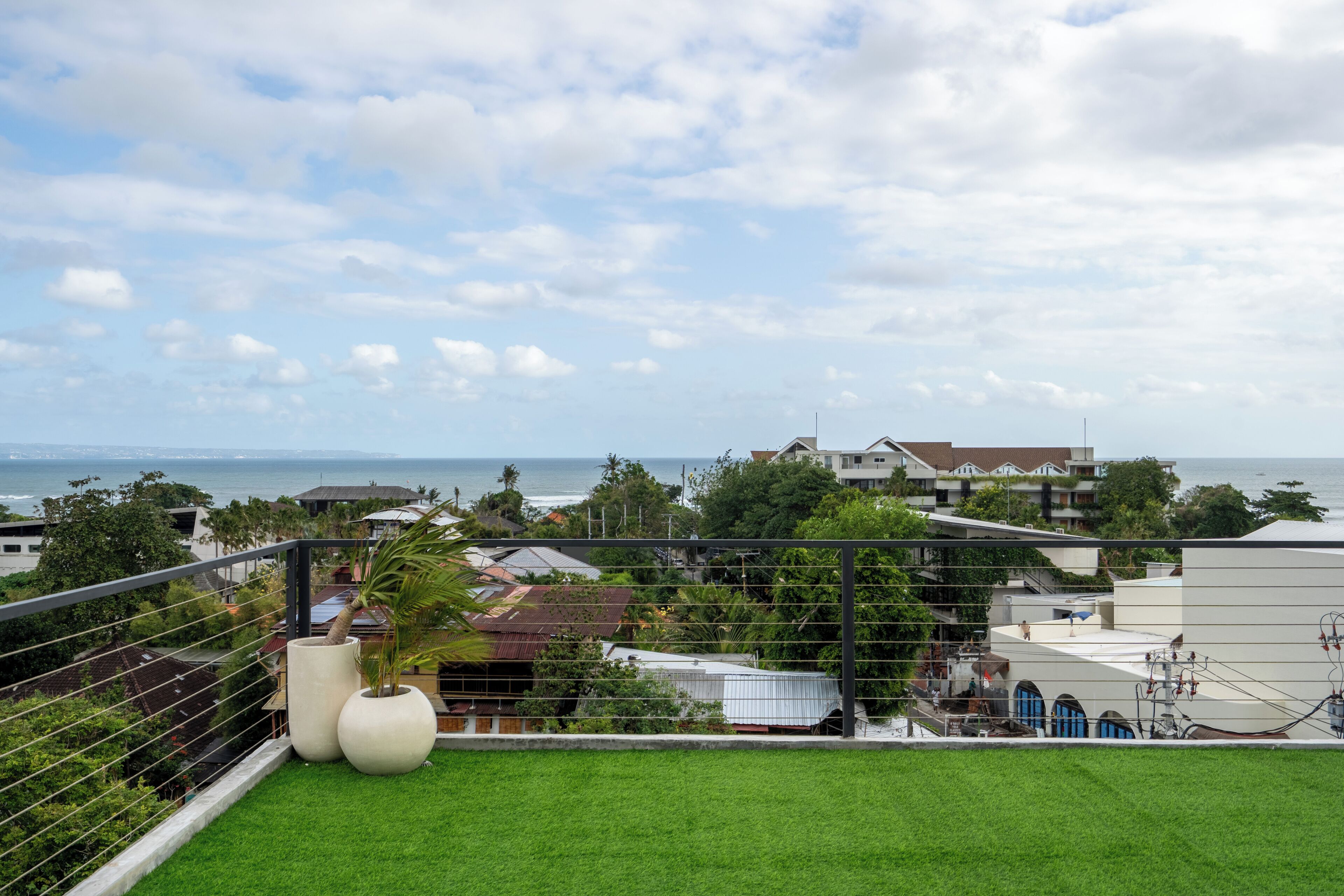 A balcony with artificial grass, a white planter, and a view of the ocean and buildings.