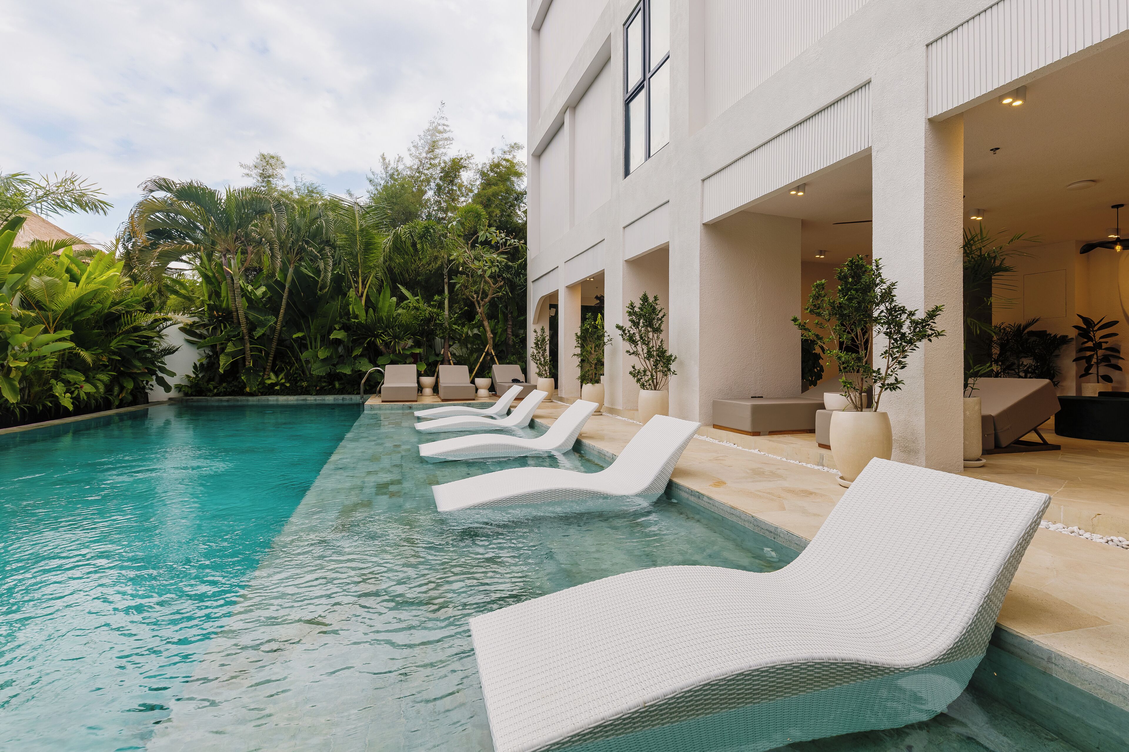 A pool area with white lounge chairs and a building with large windows and a covered patio.