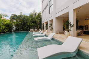 A pool area with white lounge chairs and a building with large windows and a covered patio.