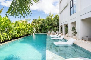 Piscina con sillones de descanso, rodeada de vegetación exuberante y un edificio moderno.