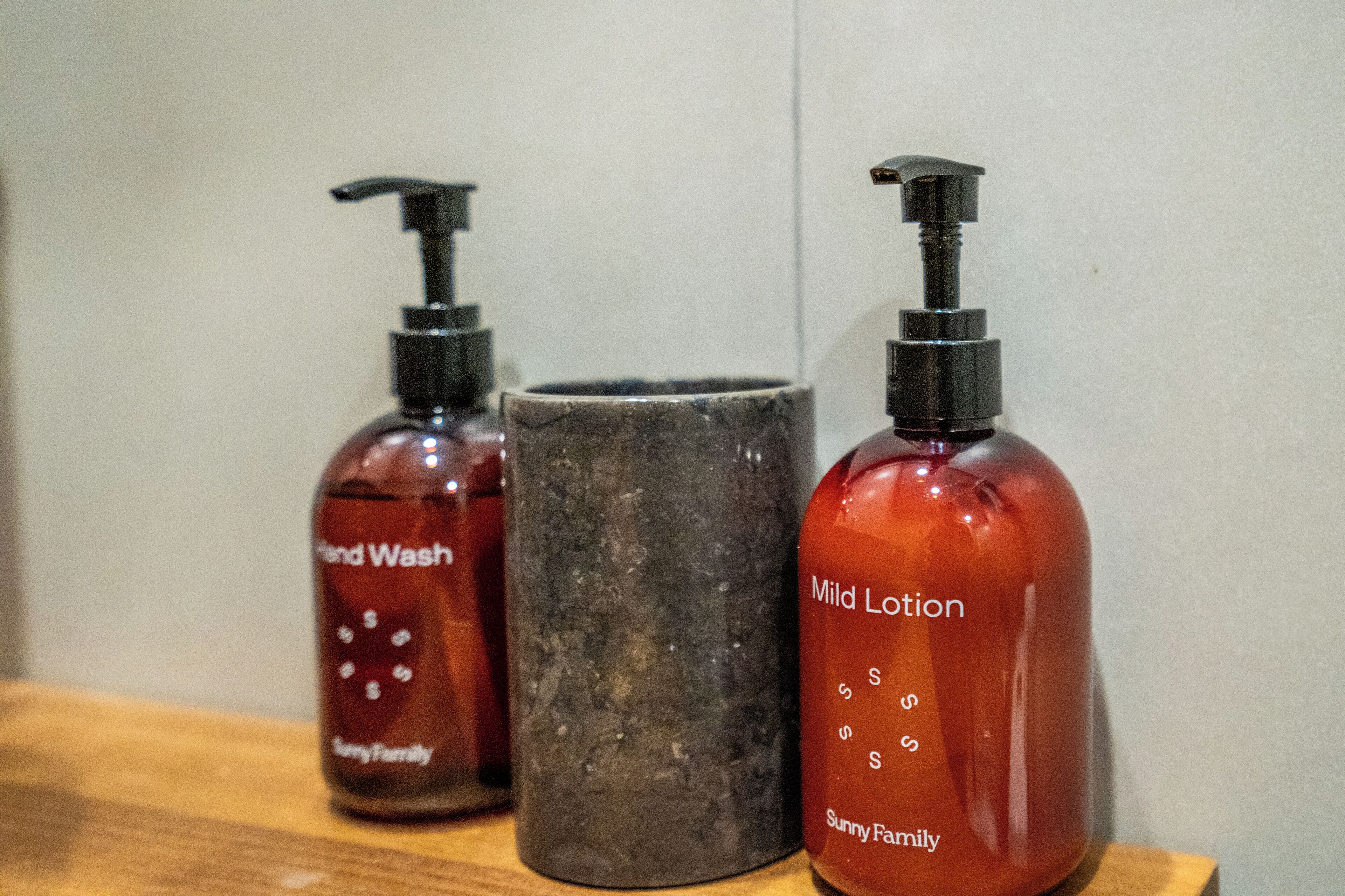 Two bottles of hand wash and mild lotion, and a dark-colored container on a wooden surface.