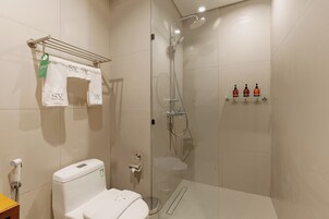 A modern bathroom with a glass-enclosed shower, a toilet, and a shelf with toiletries.