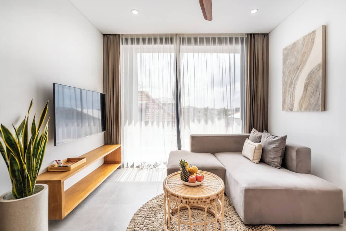A modern living room with a sofa, a coffee table with fruit, a TV, and a large window with curtains.